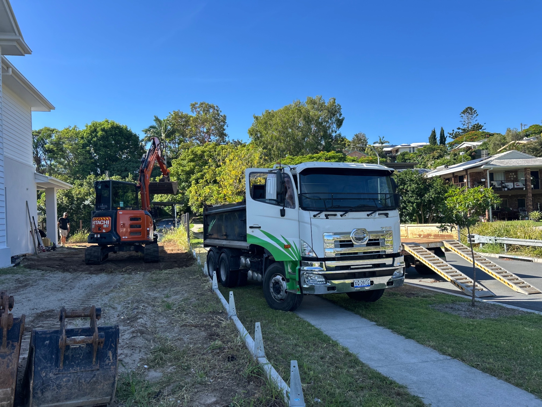 Green tipper truck parked beside an excavator on a live job site