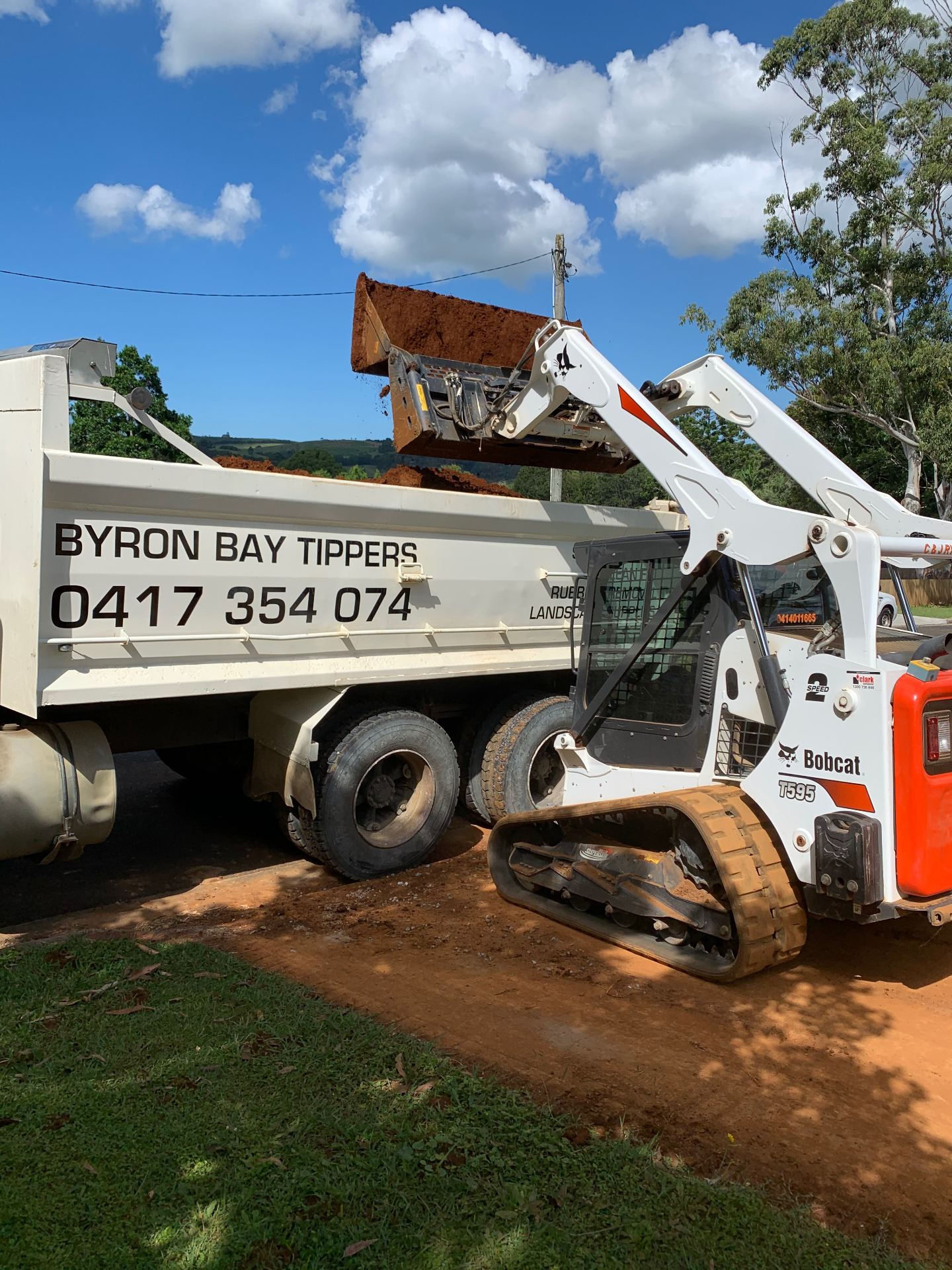 Bobcat loading red soil into a Byron Bay Tippers truck